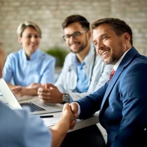 Happy businessman having a meeting with group of doctors and shaking hands with one of them in the office.